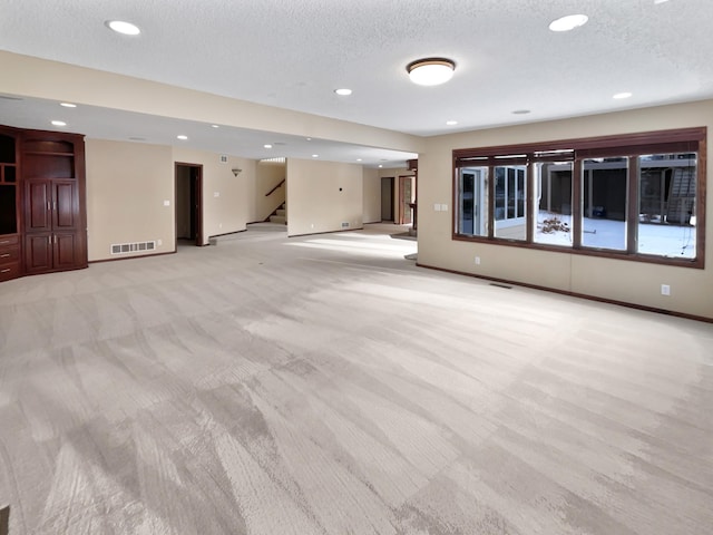 unfurnished living room with light carpet, stairway, a textured ceiling, and visible vents