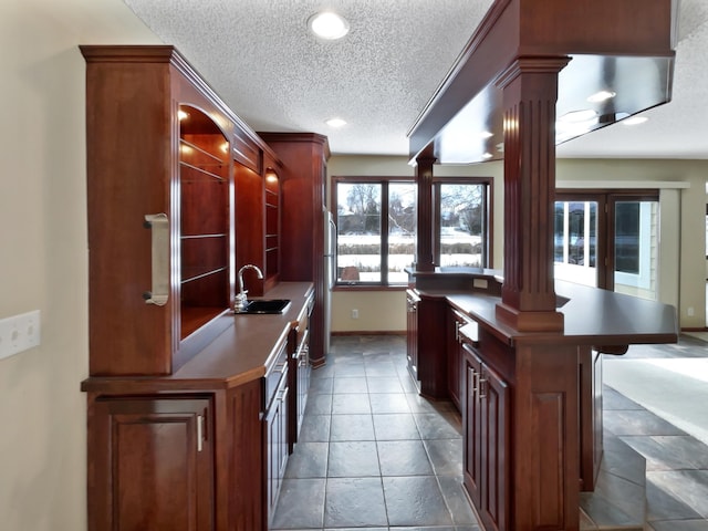 kitchen featuring dark countertops, a breakfast bar, a textured ceiling, ornate columns, and a sink