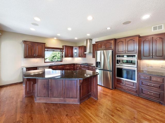 2464 Tournament Players Cir N, Blaine, MN 55449 - kitchen with appliances with stainless steel finishes, wall chimney range hood, a textured ceiling, a kitchen island, and decorative backsplash