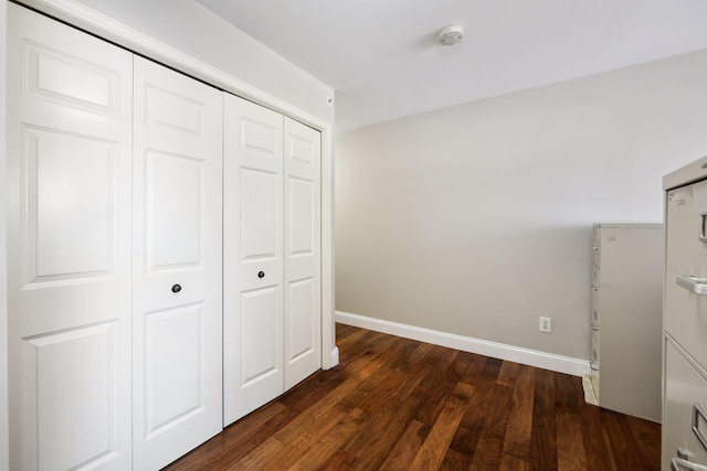 unfurnished bedroom with a closet, baseboards, and dark wood finished floors