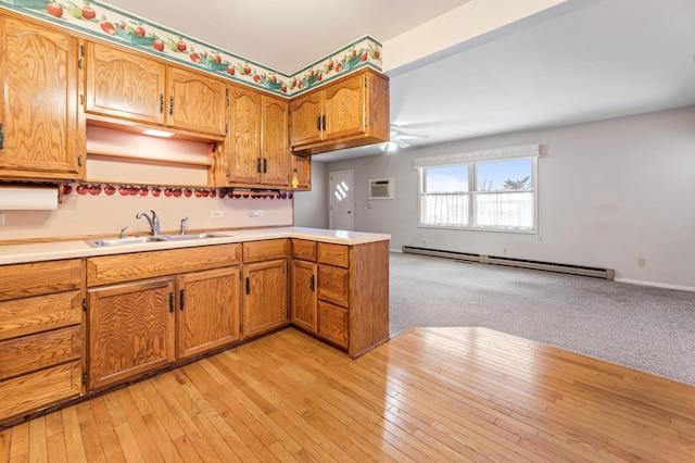 kitchen featuring light wood finished floors, brown cabinetry, a baseboard radiator, light countertops, and a sink