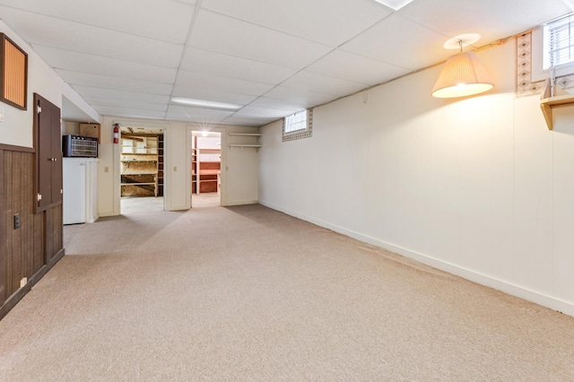 below grade area featuring carpet floors, wood walls, baseboards, and a drop ceiling