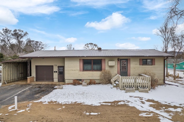 ranch-style home featuring a garage, metal roof, and driveway