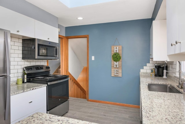 kitchen featuring stainless steel appliances, tasteful backsplash, white cabinetry, a sink, and baseboards