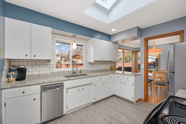 kitchen with stainless steel appliances, a skylight, a sink, white cabinetry, and tasteful backsplash