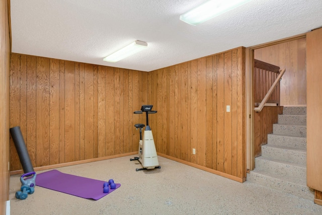 exercise room featuring a textured ceiling, wood walls, and baseboards