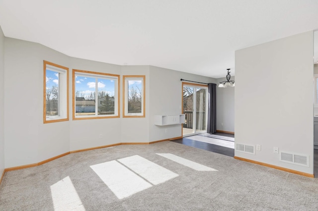 empty room featuring a chandelier, carpet flooring, visible vents, and baseboards