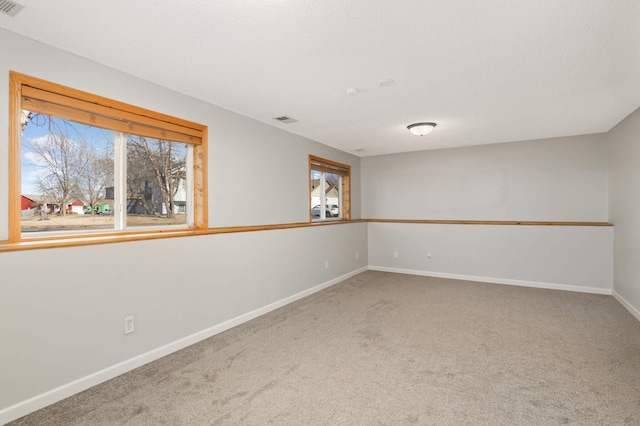 carpeted empty room featuring a wealth of natural light, visible vents, and baseboards