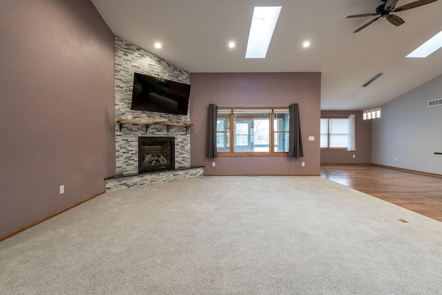 unfurnished living room with a ceiling fan, a skylight, a stone fireplace, and carpet