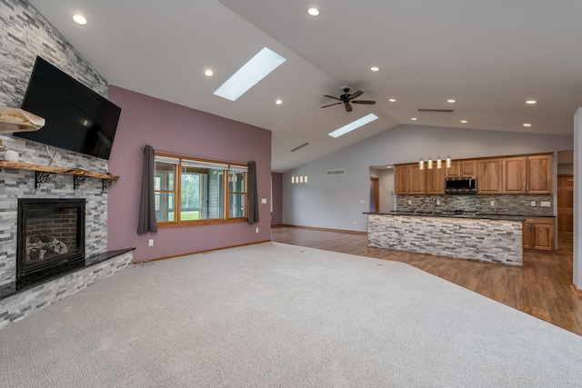 living room with a skylight, visible vents, a ceiling fan, light wood-type flooring, and a fireplace