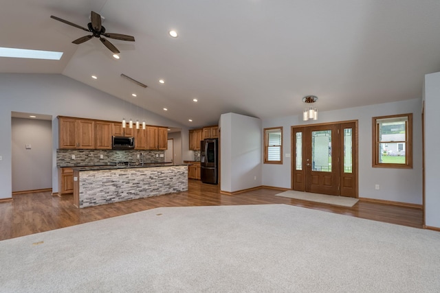 kitchen featuring stainless steel appliances, a skylight, open floor plan, backsplash, and dark countertops