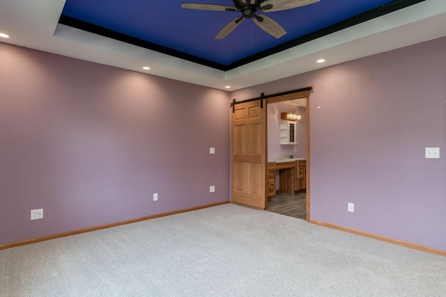 carpeted spare room featuring recessed lighting, a raised ceiling, a barn door, a ceiling fan, and baseboards