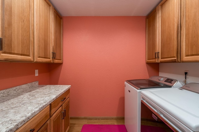 clothes washing area with light wood-type flooring, washing machine and dryer, cabinet space, and baseboards