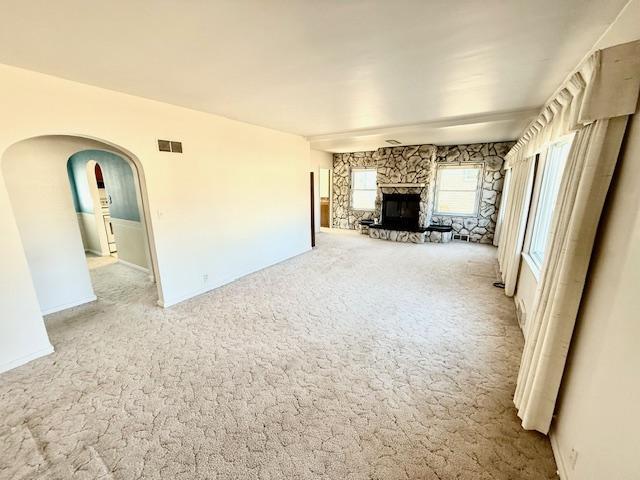 unfurnished living room with arched walkways, visible vents, a fireplace, and carpet flooring