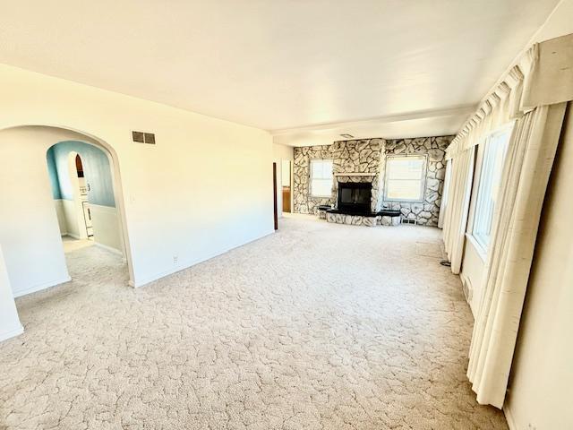 unfurnished living room featuring visible vents, arched walkways, carpet flooring, and a stone fireplace