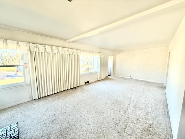 unfurnished room with baseboards, carpet, visible vents, and beam ceiling