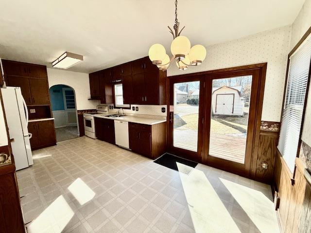 kitchen featuring arched walkways, light floors, light countertops, white appliances, and wallpapered walls