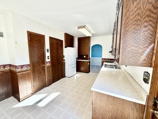 kitchen featuring arched walkways, light floors, light countertops, freestanding refrigerator, and a sink