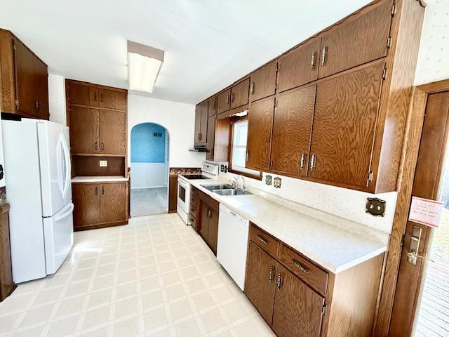 kitchen with white appliances, arched walkways, light countertops, light floors, and a sink