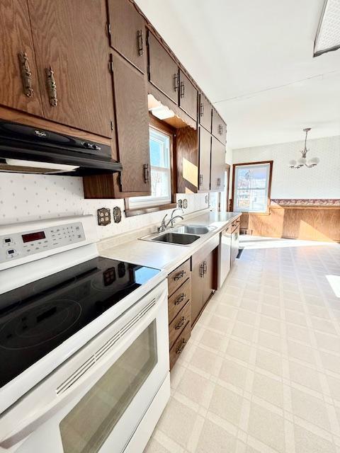 kitchen featuring under cabinet range hood, light countertops, white electric range, light floors, and a sink