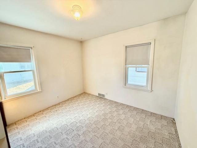 carpeted empty room featuring visible vents and plenty of natural light