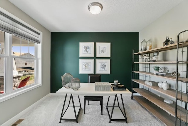 carpeted home office with an accent wall, visible vents, and baseboards