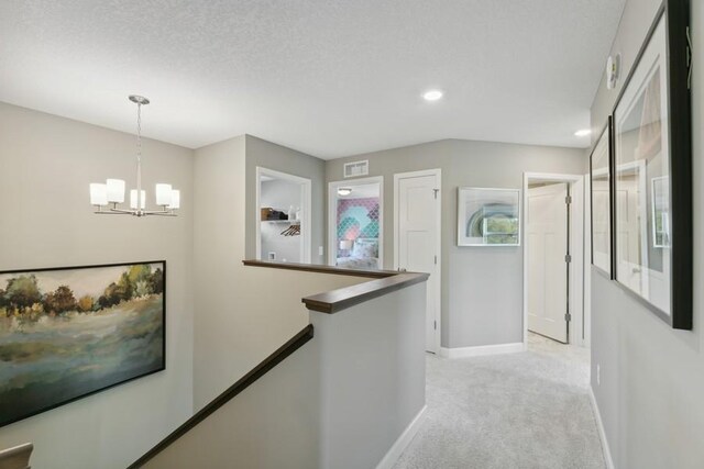 hallway with light carpet, visible vents, an upstairs landing, baseboards, and an inviting chandelier