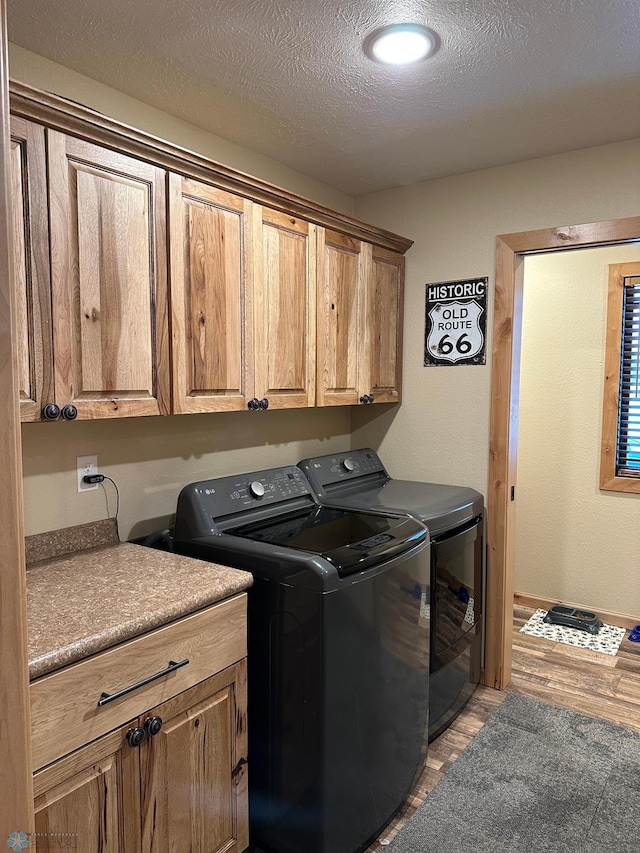 washroom featuring a textured ceiling, washer and clothes dryer, cabinet space, and light wood-style floors