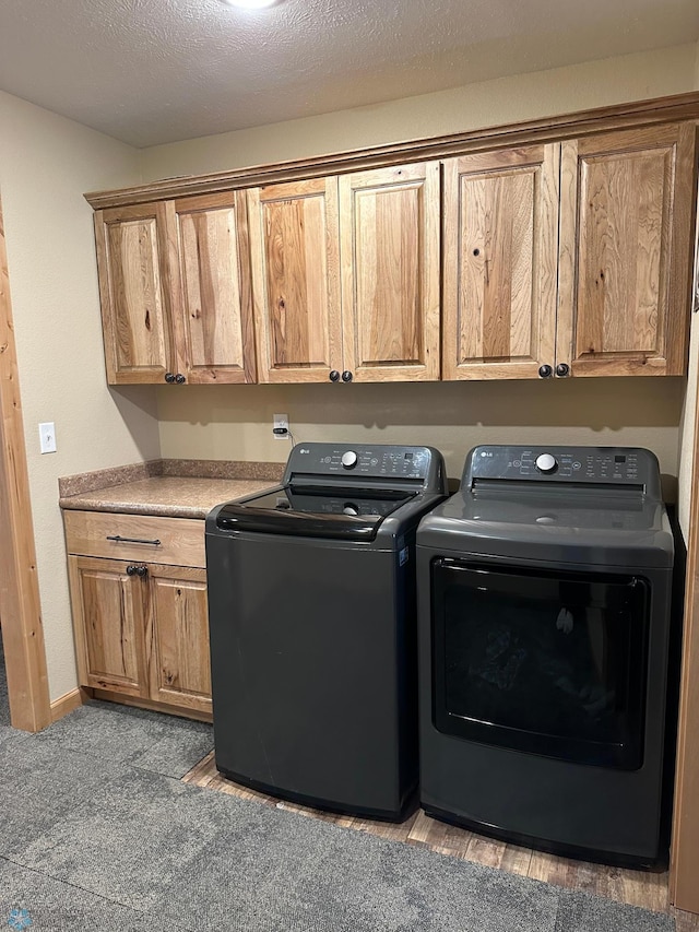 clothes washing area with a textured ceiling, separate washer and dryer, cabinet space, and baseboards