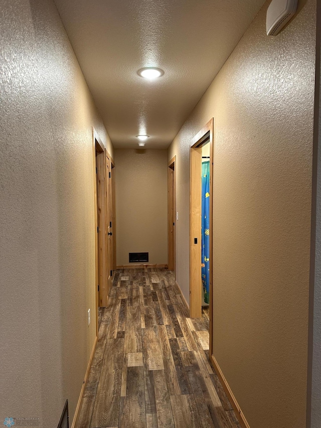 hall featuring baseboards, visible vents, dark wood finished floors, and a textured wall