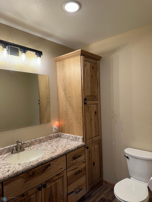 half bathroom with a textured wall, toilet, wood finished floors, a textured ceiling, and vanity