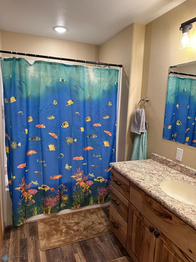 full bathroom featuring a textured wall, a shower with curtain, wood finished floors, and vanity