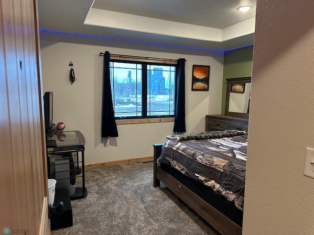 carpeted bedroom with a raised ceiling and baseboards