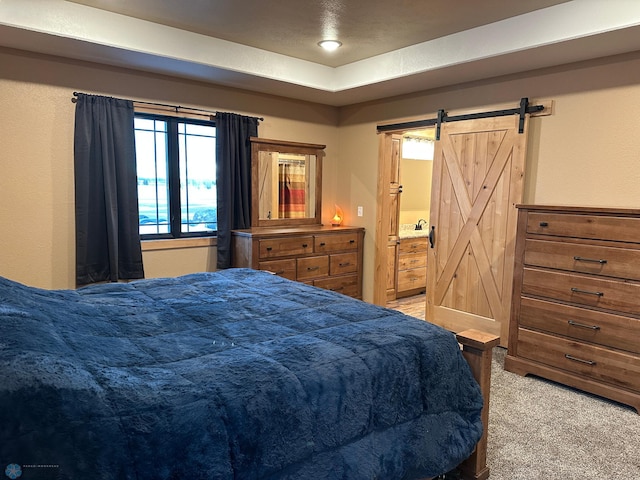 bedroom with light colored carpet, connected bathroom, and a barn door