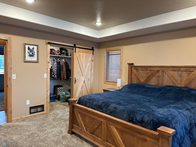 bedroom featuring a barn door, a spacious closet, visible vents, and carpet flooring