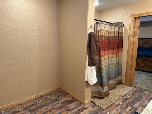 full bath featuring a textured wall, baseboards, and wood finished floors