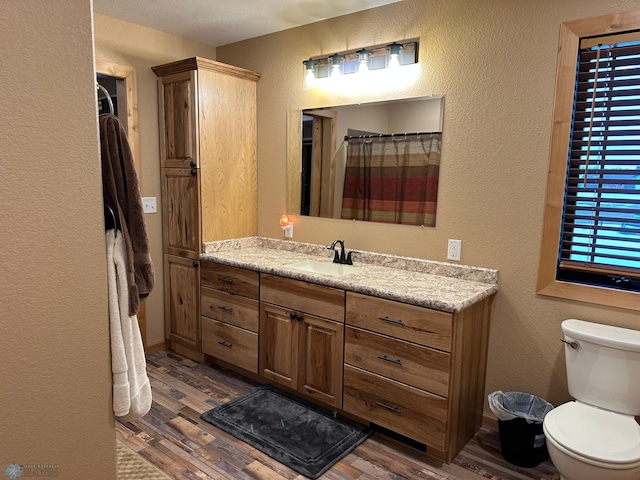 full bath featuring a textured wall, vanity, toilet, and wood finished floors