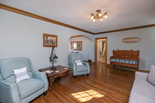 living room featuring ornamental molding, a textured ceiling, wood finished floors, arched walkways, and baseboards