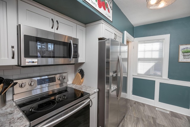 kitchen featuring backsplash, white cabinets, stainless steel appliances, and light stone countertops