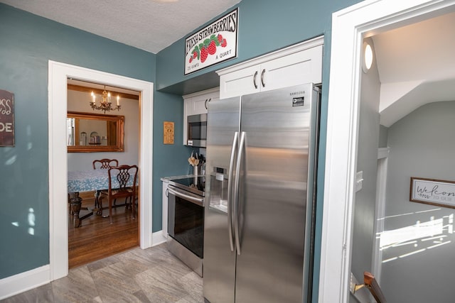 kitchen featuring baseboards, a chandelier, stainless steel appliances, white cabinets, and a textured ceiling