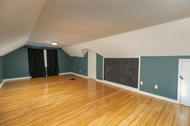 bonus room featuring baseboards, visible vents, lofted ceiling, light wood-style floors, and a textured ceiling