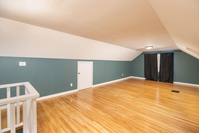 bonus room with visible vents, lofted ceiling, light wood-style flooring, a textured ceiling, and baseboards