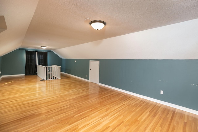 bonus room featuring a textured ceiling, lofted ceiling, baseboards, and wood finished floors