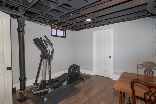 exercise room with visible vents, concrete block wall, and dark wood-style flooring