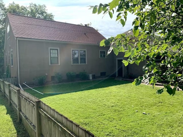 rear view of house featuring a lawn, fence, roof with shingles, and stucco siding