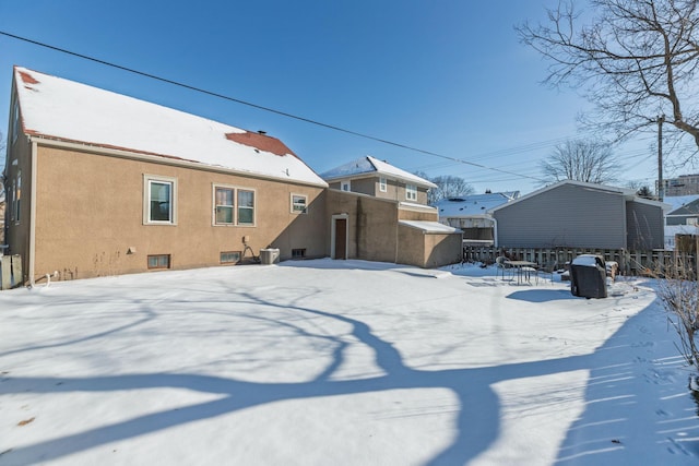 snow covered property featuring fence, central AC, and stucco siding