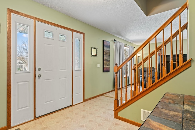 foyer with stairway, visible vents, a textured ceiling, and baseboards