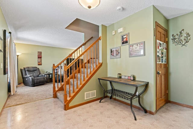 staircase with a textured ceiling, visible vents, and baseboards