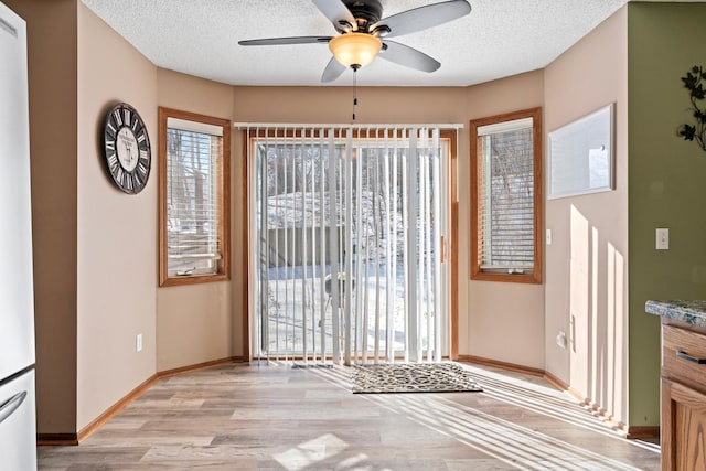 dining space with a textured ceiling, ceiling fan, baseboards, and light wood-style floors