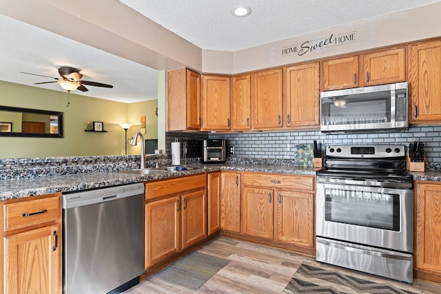 kitchen featuring stainless steel appliances, dark stone counters, a sink, and backsplash